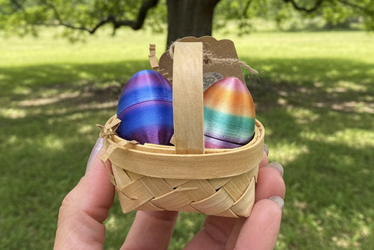 Hand holding a small woven basket with colorful eggs outdoors.